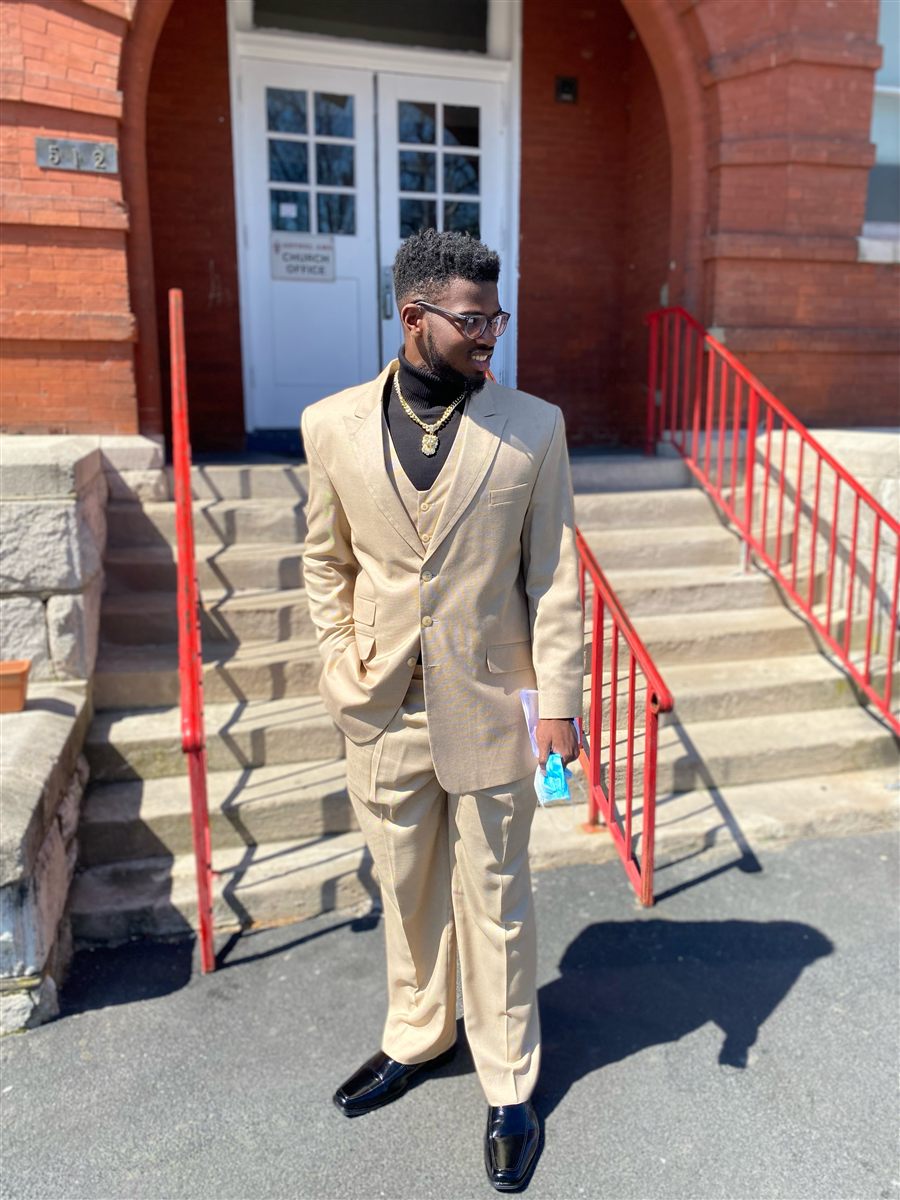 Isaiah Marshall in a tan suit standing in front of a brick building